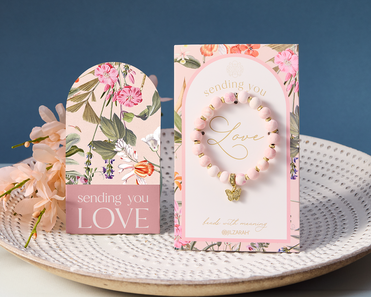 The Blush Sending You Love bracelet on its floral card, with the blank gift note card standing beside it on a white plate