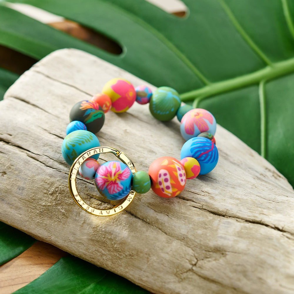 Paradise Island wrist keychain resting on driftwood with green leaves